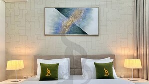 Une chambre d’hôtel comprenant un lit, deux tables de chevet, deux lampes et un tableau abstrait accroché au mur.