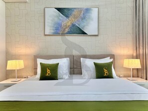 A hotel room with a bed, two nightstands, two lamps, and a wall-mounted abstract painting. - Amazing Water View Luxury 2 Br Prime Location (Dubai)