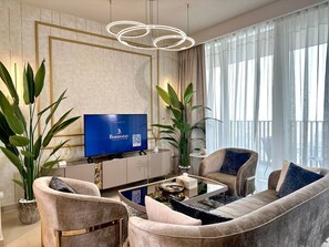 A modern living room with a large flat-screen TV, comfortable seating, and large windows. - Amazing Water View Luxury 2 Br Prime Location (Dubai)