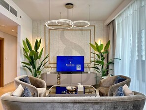 Una sala de estar moderna con una televisión de pantalla plana, dos sillones, una mesa de centro y plantas verdes grandes.