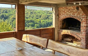 Un espace extérieur aménagé dans un style rustique, avec une cheminée en briques, des bancs en bois et une vue sur un paysage boisé.