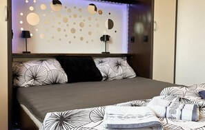A neatly made bed with patterned bedding, a wall with circular cutouts, and two bedside lamps. - Nice home in Donji Kraljevec with WiFi (Donji Kraljevec)