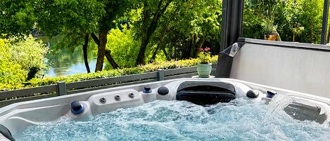 A hot tub with a view of a lush garden and a body of water.