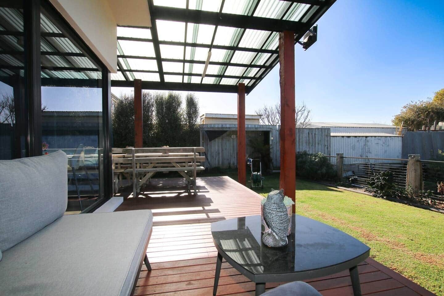 A covered patio area with a glass table, a bench, and a sofa.