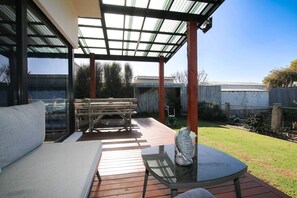 A covered patio area with a glass table, a bench, and a sofa. - 'The Wetlands' Holiday Home (Warrnambool)