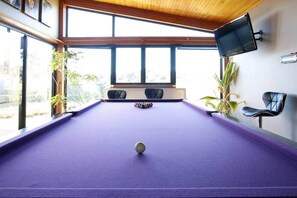 A pool table with a ball in the center, surrounded by chairs and potted plants. - 'The Wetlands' Holiday Home (Warrnambool)