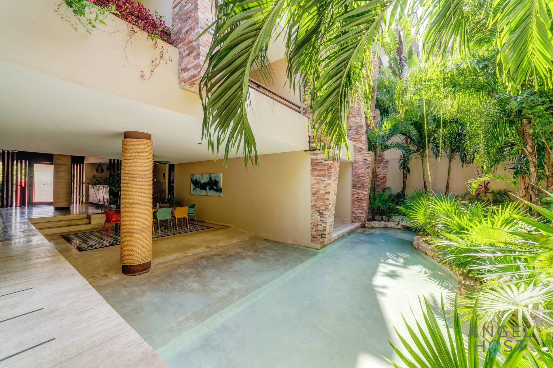 A spacious indoor area with a pool, surrounded by lush greenery and a dining area with chairs.