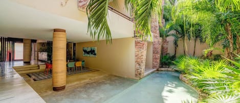 A spacious indoor area with a pool, surrounded by lush greenery and a dining area with chairs.