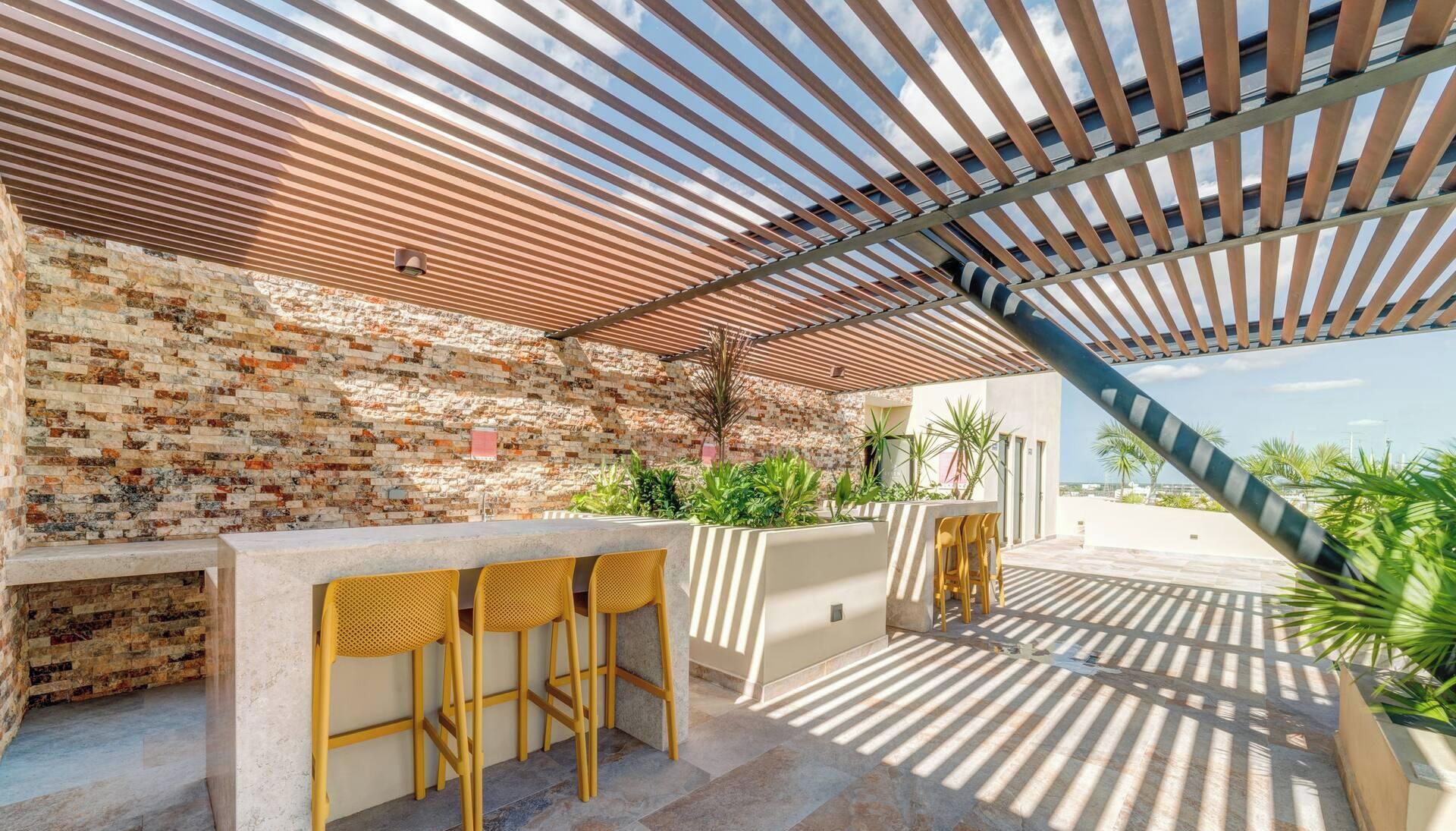 An outdoor patio with a brick wall, a wooden pergola, and a seating area with chairs.
