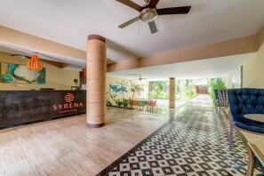 A hotel lobby with a reception desk, a large pillar, a ceiling fan, and a view of the outdoor area. - Syrena studio w/ rooftop pool near beach (Playa del Carmen)