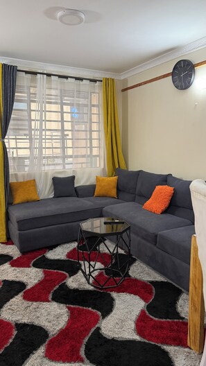 A living room with a sectional sofa, a glass coffee table, and a patterned rug. - Couch Potato Pad - Tripple R Ruaka (Ruaka)