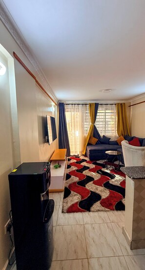 A living room with a sofa, a coffee table, a TV, and a small table with a plant. - Couch Potato Pad - Tripple R Ruaka (Ruaka)