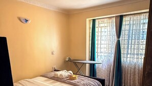 Un dormitorio con una cama, un tapete rojo, una mesita pequeña y una ventana con cortinas.