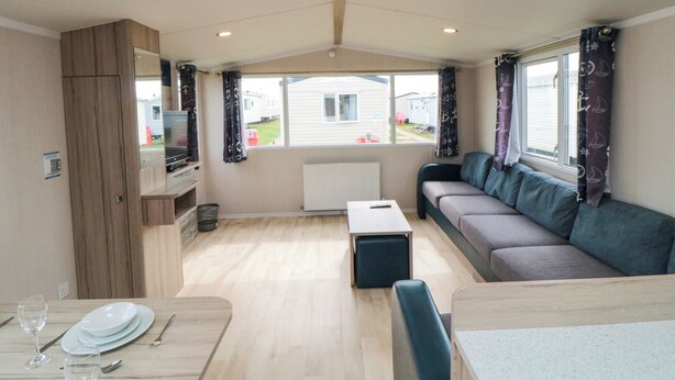 Interiør i en campingvogn med spiseplads, sofa og TV.