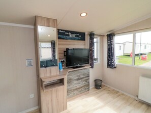 A compact living space with a television, a mirror, and a window with curtains. - 42 Oak Green (Filey)