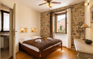 Ein Schlafzimmer mit einem hölzernen Bett, Deckenventilator, Steinwand, einem Fenster mit Vorhängen und Nachttischlampen.