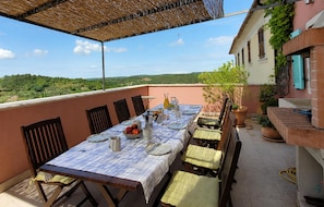 Ein Essbereich im Freien mit einem Tisch für vier Personen, umgeben von Stühlen, auf einer Terrasse mit Blick ins Grüne.