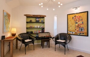 Ein Zimmer mit einem Holztisch, zwei schwarzen Ledersesseln, einem Bücherregal, einer Karte und einem großen gerahmten Kunstwerk.