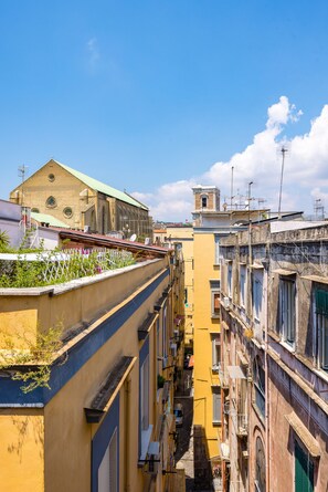Un vicolo stretto tra edifici con balconi, una chiesa con un tetto verde e un cielo azzurro limpido.