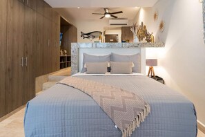 Ein Schlafzimmer mit einem Bett, einem Deckenventilator, einem Nachttisch und einem an der Wand befestigten Regal.