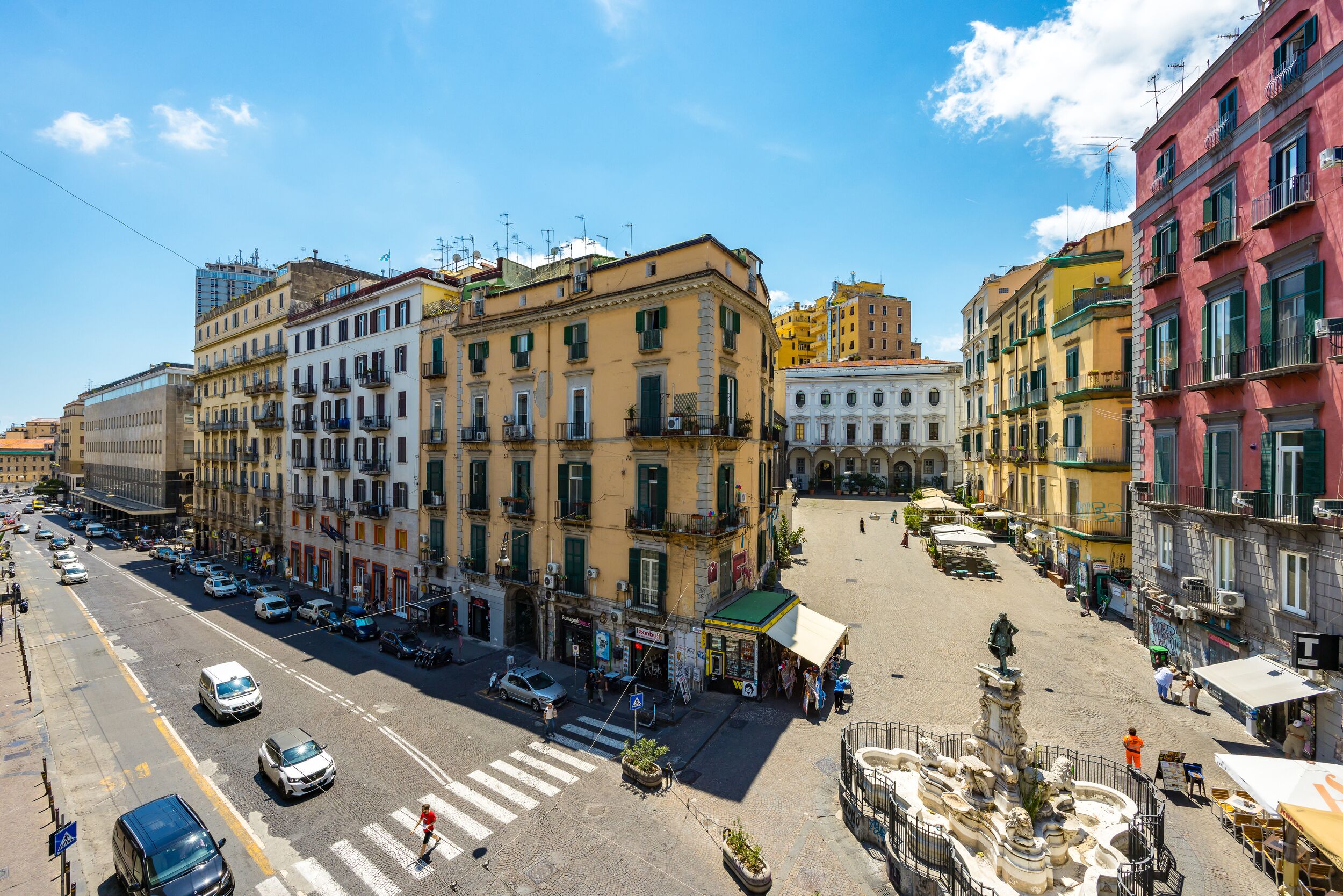 A street view of a city with buildings, a pedestrian crossing, and a statue in the foreground.