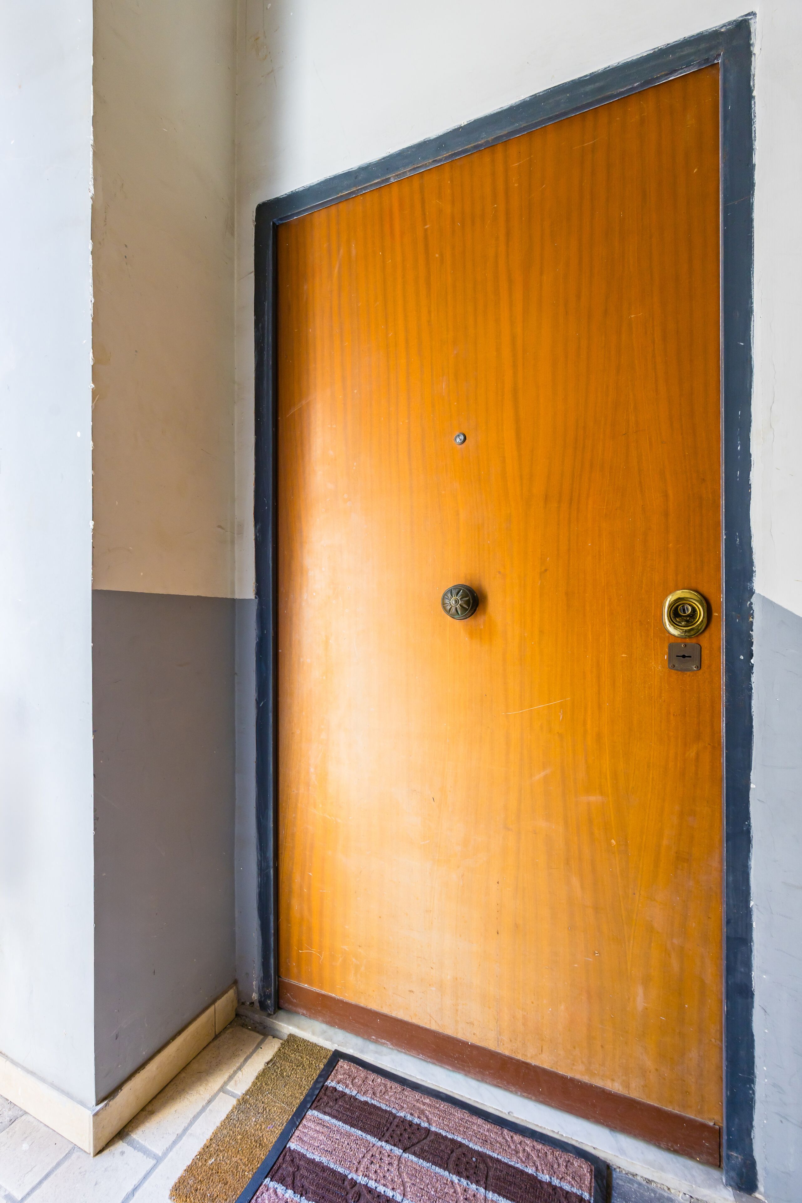 A wooden door with a brass doorknob and a keyhole, set in a corner with a white wall and a brown baseboard.