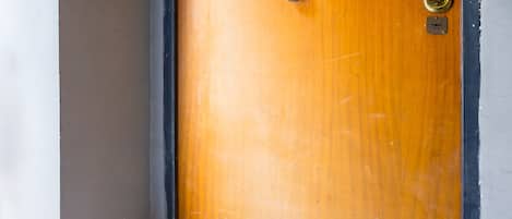 Una puerta de madera con un picaporte de latón y un ojo de cerradura, ubicada en una esquina con una pared blanca y un zócalo marrón.