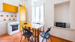 A compact kitchen with a stove, oven, and microwave. There is a dining table with chairs and a window providing natural light. - Pizzarchouse (Naples)