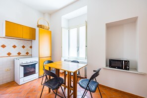 Eine kompakte Küche mit Herd, Backofen und Mikrowelle. Ein Esstisch mit Stühlen und ein Fenster sorgen für natürliches Licht.