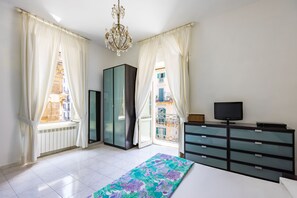 Une chambre à coucher avec un lit, une commode, un téléviseur et une vue sur les immeubles par la fenêtre.