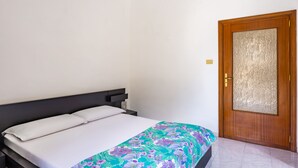 A single bed with a white mattress and a floral-patterned blanket, a dark headboard, and a wooden door with a textured glass panel. - Pizzarchouse (Naples)