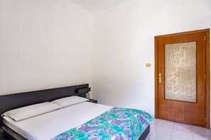 Ein Einzelbett mit weißer Matratze und einer Decke mit Blumenmuster, ein dunkles Kopfteil und eine Holztür mit einem satinierten Glasfenster.