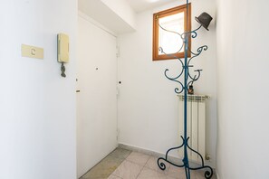 Un couloir avec une porte blanche, un téléphone fixé au mur, un radiateur et un présentoir métallique décoratif sur lequel est posé un chapeau.
