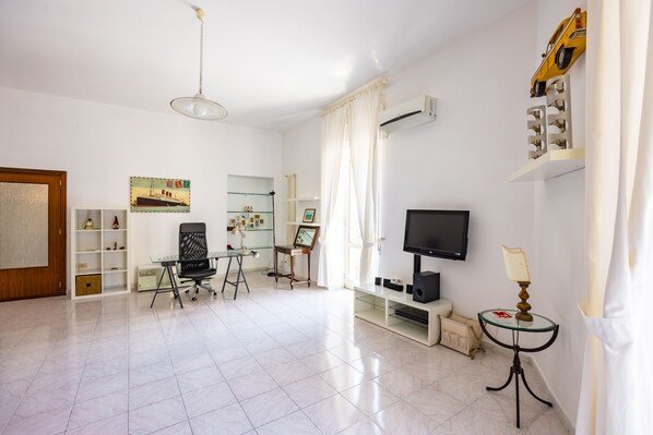 A spacious living room with a flat-screen TV, a glass coffee table, and a comfortable seating area. - Pizzarchouse (Naples)