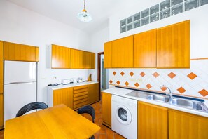 A compact kitchen with wooden cabinets, a built-in washing machine, and a tiled backsplash. - Pizzarchouse (Naples)