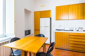 A compact kitchen with wooden cabinets, a white refrigerator, a microwave, and a dining table with chairs. - Pizzarchouse (Naples)