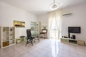 Ein modernes Wohnzimmer mit einem Glastisch, einem schwarzen Bürostuhl, einem Flachbildfernseher und einer Heizung.