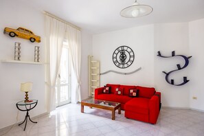 Ein Wohnzimmer mit rotem Sofa, Couchtisch, Wanduhr, Heizkörper und einem fenster mit Vorhängen.