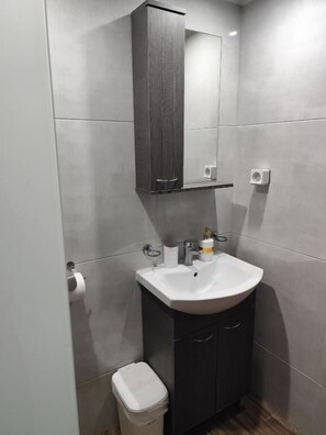 A bathroom with a white sink, dark cabinets, a mirror, and a toilet. - Beachfront Kala's Suites Apartments (Ammoudara Heraklion)