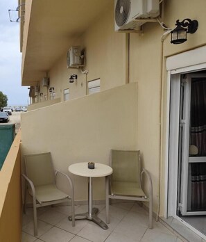 A balcony with two chairs and a small table, an air conditioning unit, and a sliding glass door. - Beachfront Kala's Suites Apartments (Ammoudara Heraklion)
