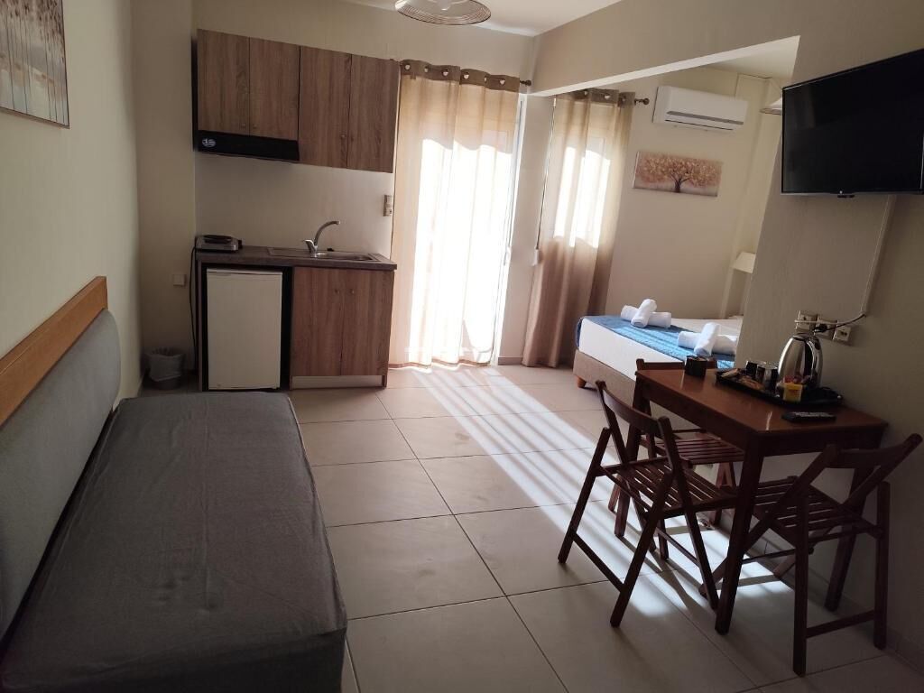 A compact hotel room with a kitchenette, a bed, a desk with chairs, and a television.