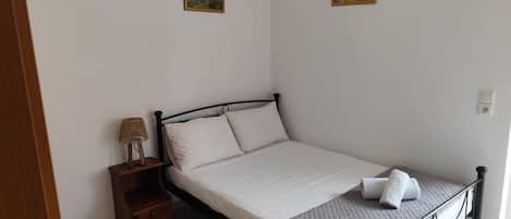 Una cama individual con estructura metálica, una mesita de noche de madera con lámpara, y dos cuadros en la pared.