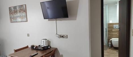 Una habitación con una mesa de comedor, sillas, un televisor de pantalla plana montado en la pared y un acceso a un baño.