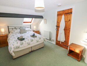 A bedroom with a bed, bedside tables, a radiator, a wooden door, and a skylight. - Barn Cottage (Haverfordwest)