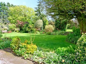 A garden with a lawn, various plants, a bench, and a stone pathway. - Barn Cottage (Haverfordwest)