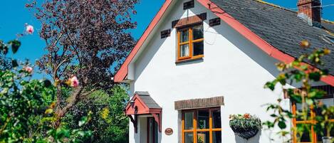 Un bâtiment blanc avec un toit rouge, une cheminée et une fenêtre agrémentée d’une jardinière.
