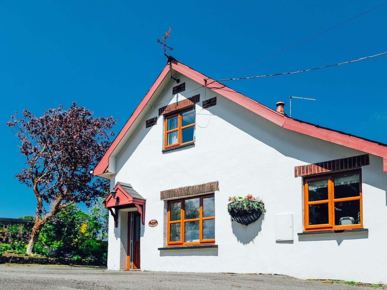 A white building with a red roof, two windows with wooden frames, and a small porch.