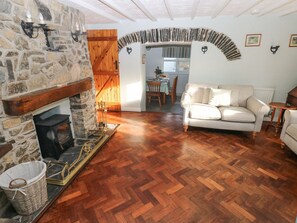 Un salón acogedor con chimenea de piedra, suelo de madera, un sofá y un área de comedor visible a través de un arco.