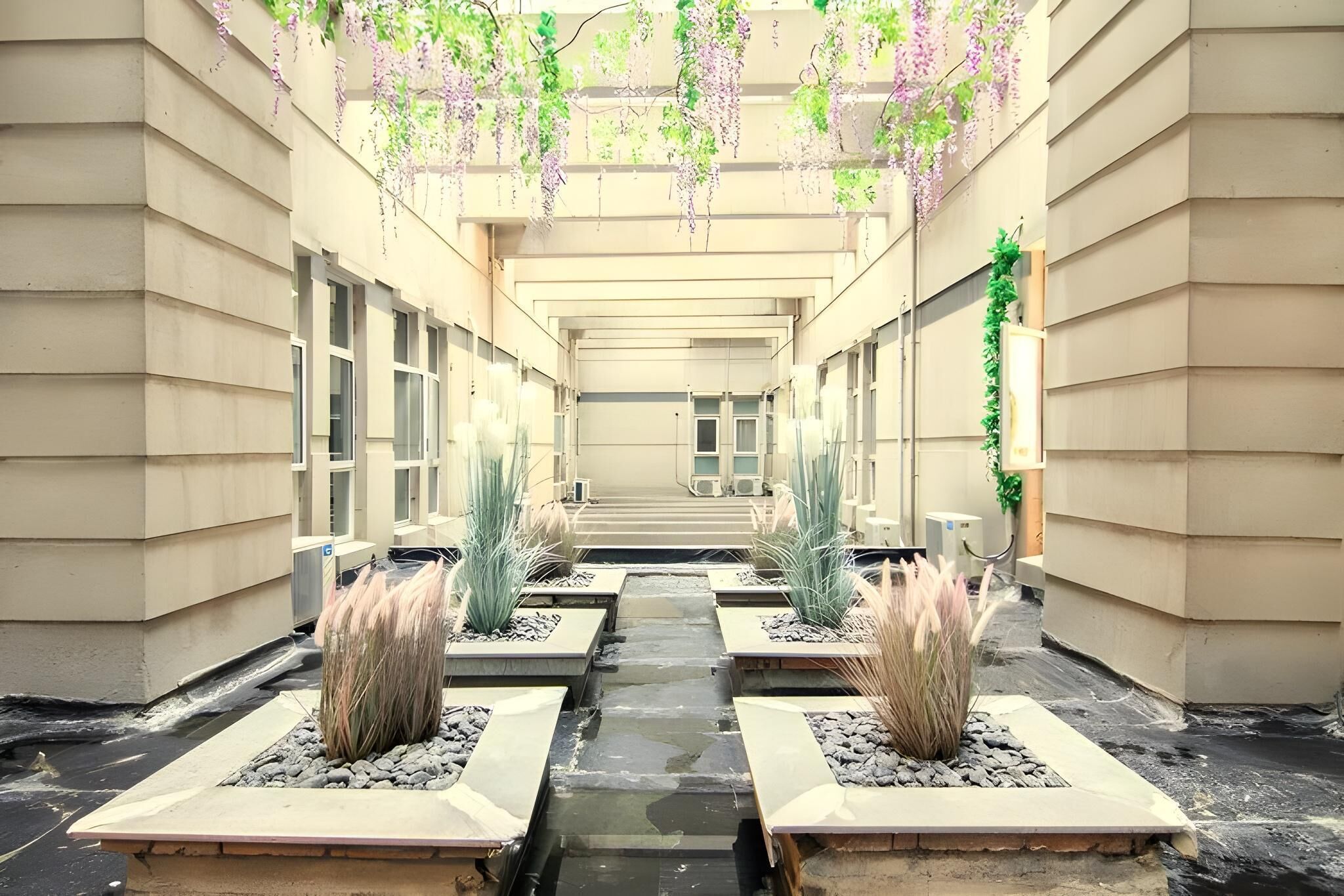A corridor with a water feature, planters, and hanging plants.