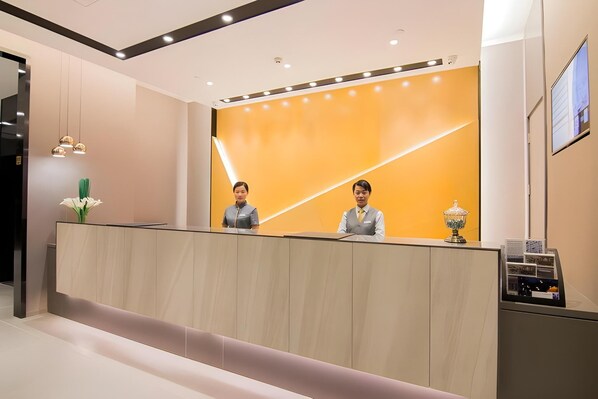 A reception desk with two staff members, a modern interior design, and a digital display.